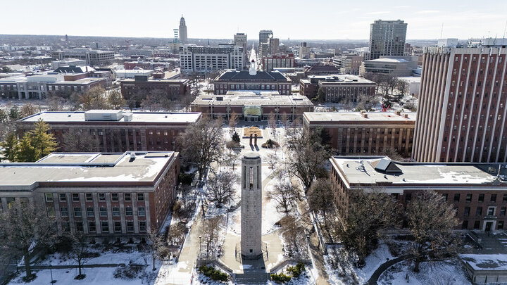 A south-facing drone shot of the city campus bell tower and the surrounding campus that is lightly dusted with snow